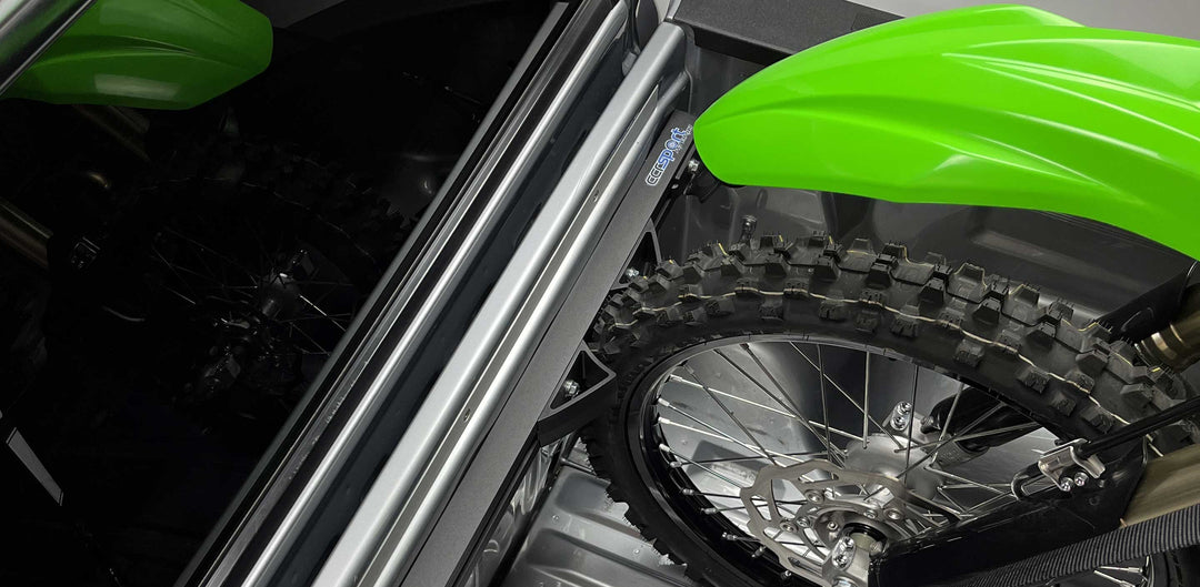 A dirt bike front tire supported by a wheel chock in a truck bed.