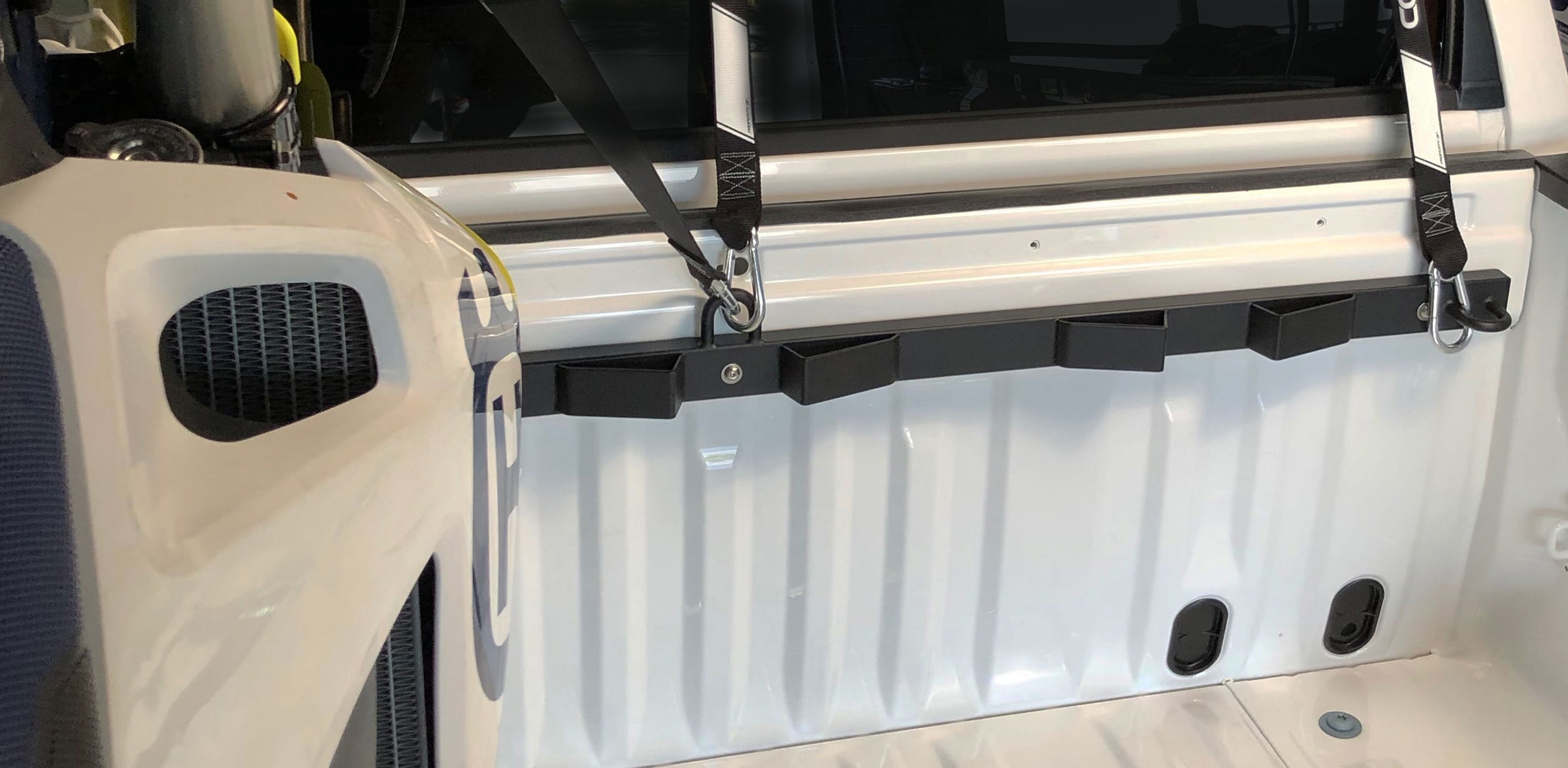 A black motorcycle tie down carrier rack mounted to a truck bed with a single motorcycle strapped into the bed of a white truck.