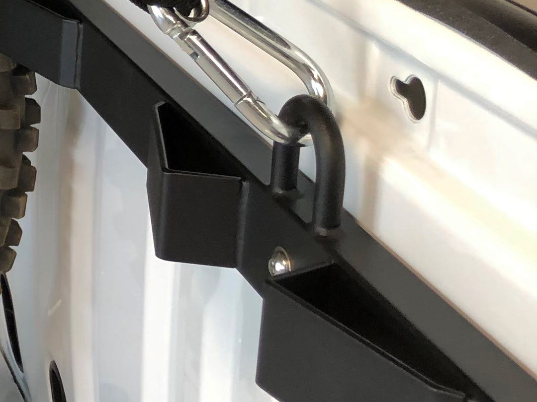 Close-up detail view of the Bed Buddy Moto Rack wheel slot and tie down loop with a carabiner strap attached.
