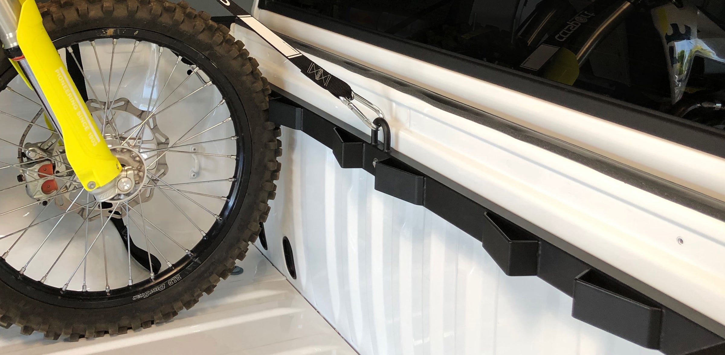 A Bed Buddy Motorcycle Tie Down Truck rack mounted in a white truck bed with a dirt bike supported in the rack for transport.