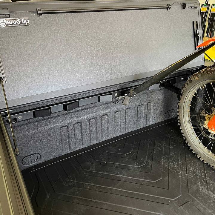 This image shows a Bed Buddy Offset Wheel Chock with a dirt bike offset from a BakFlip truck bed cover.