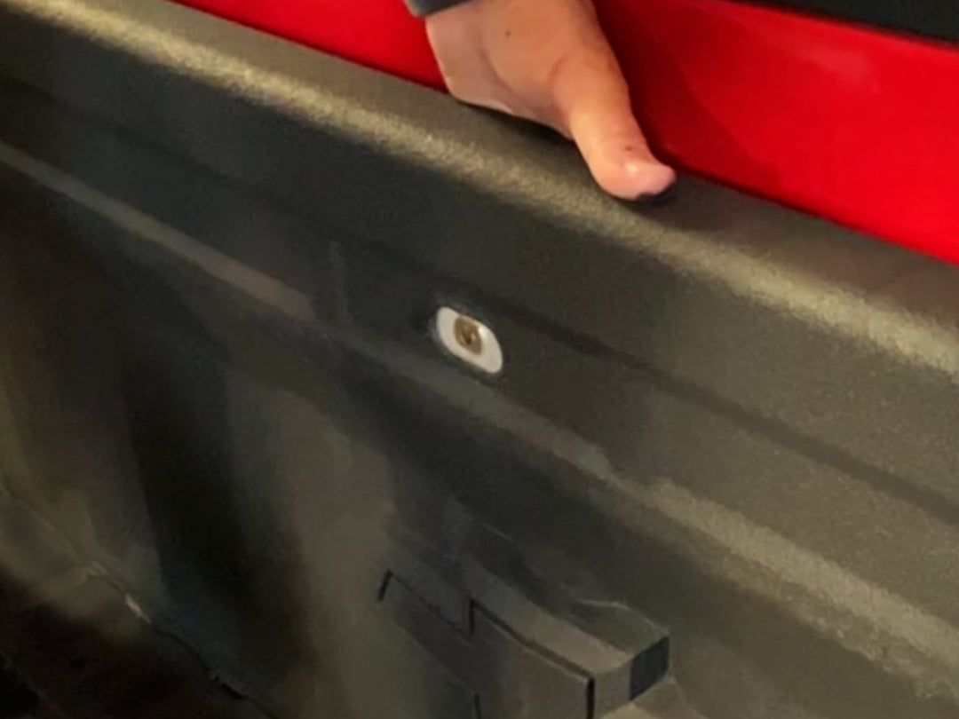 Showing a a hand between the bed and cab installing a Chevrolet / GMC backing plate.