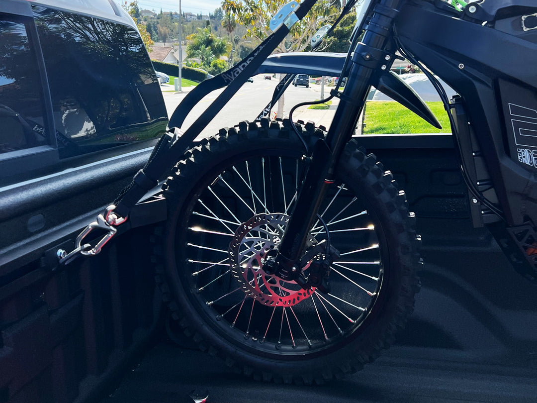 An E-Dirt Bike loaded into the bed of a truck and strapped down to a motorcycle tie down rack.