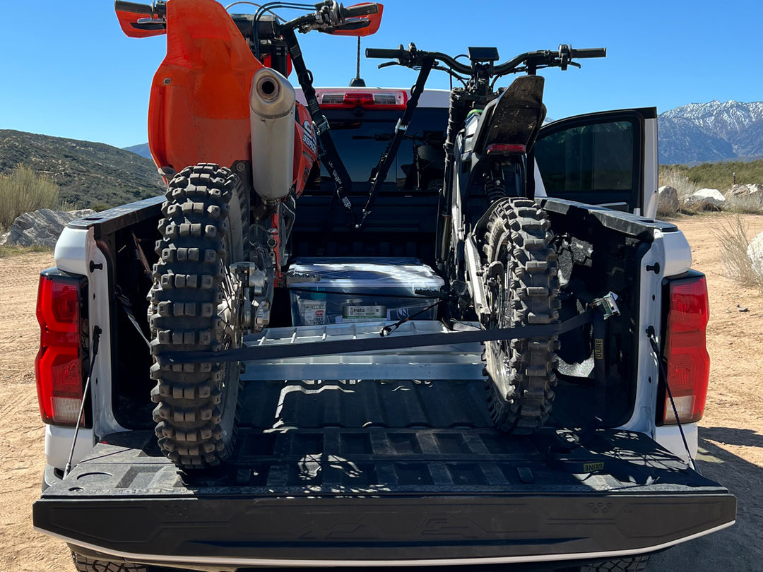 An off road dirt bike and an E-motorcycle tied down in the bed of a truck.