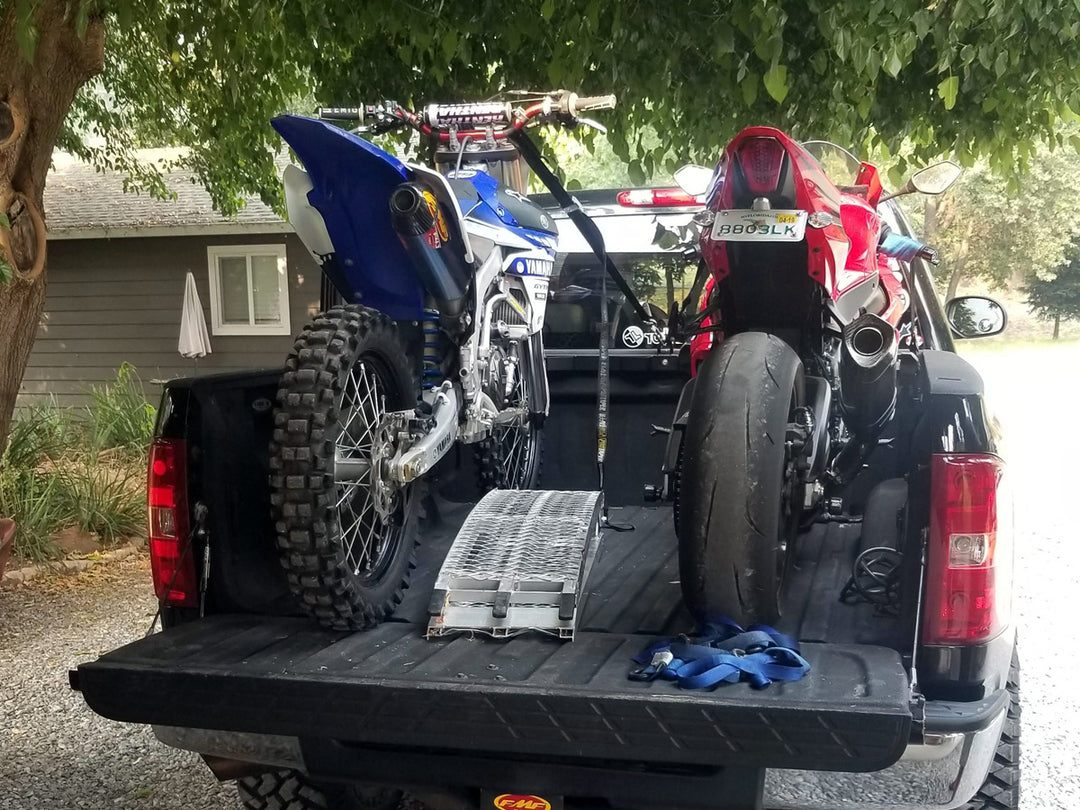 A dirt bike and a sport bike loaded into the bed of a truck and tied down for transport.