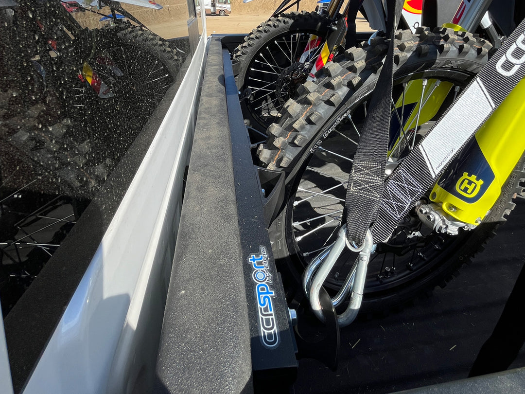 Close-up side view of the front wheel of a dirt bike supported by the Moto Vise wheel chock in a Chevy Silverado.
