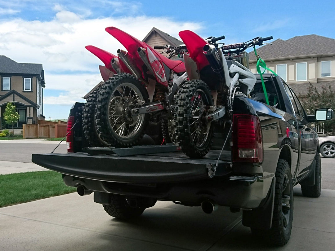 Three motocross dirt bikes loaded into the bed of a Dodge Ram ruck.