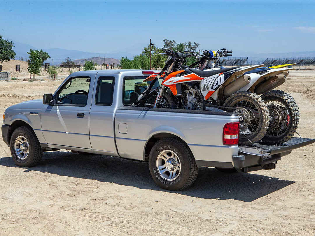 Three motocross dirt bikes loaded in the bed of a Ford Ranger.