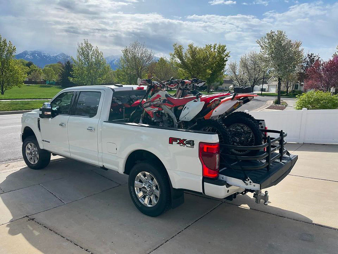 A Ford FX4 Super Duty truck with two Honda dirt bikes tie down in the truck bed.