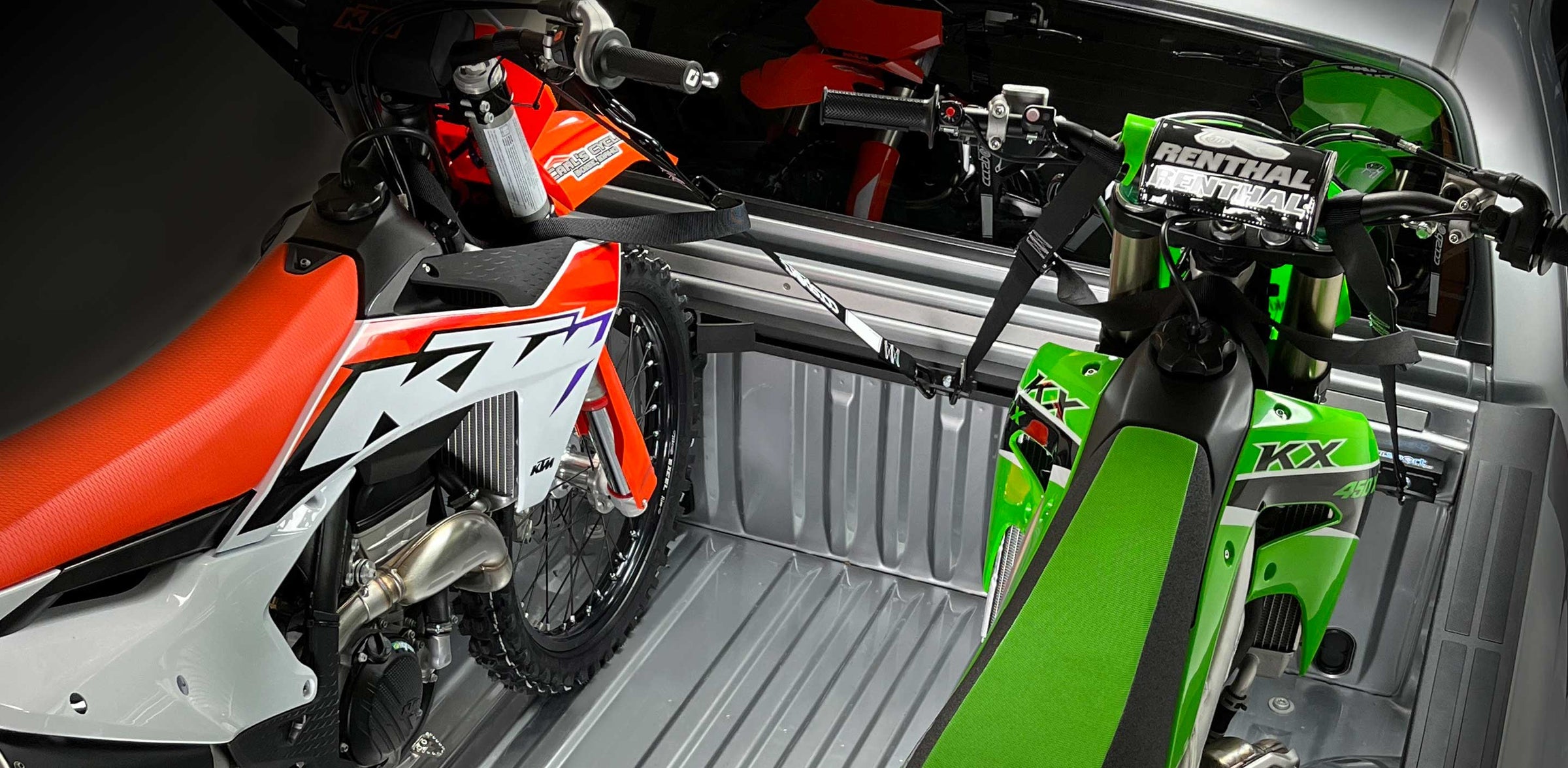 A stunning studio shot of a KTM and Kawasaki dirt bike secured to the Hybrid Moto Rack in the bed of a truck.