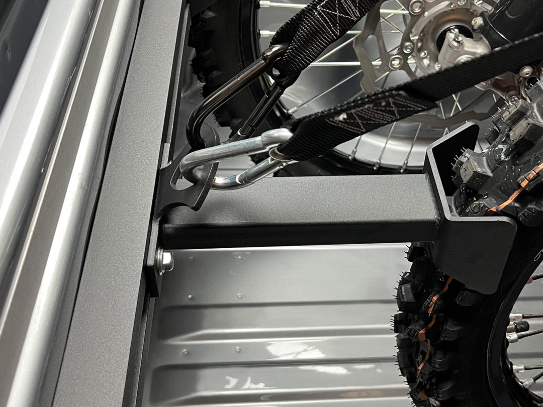 Close-up of a motorcycle being secured to the back of a vehicle with straps attached to the offset wheel chocks.