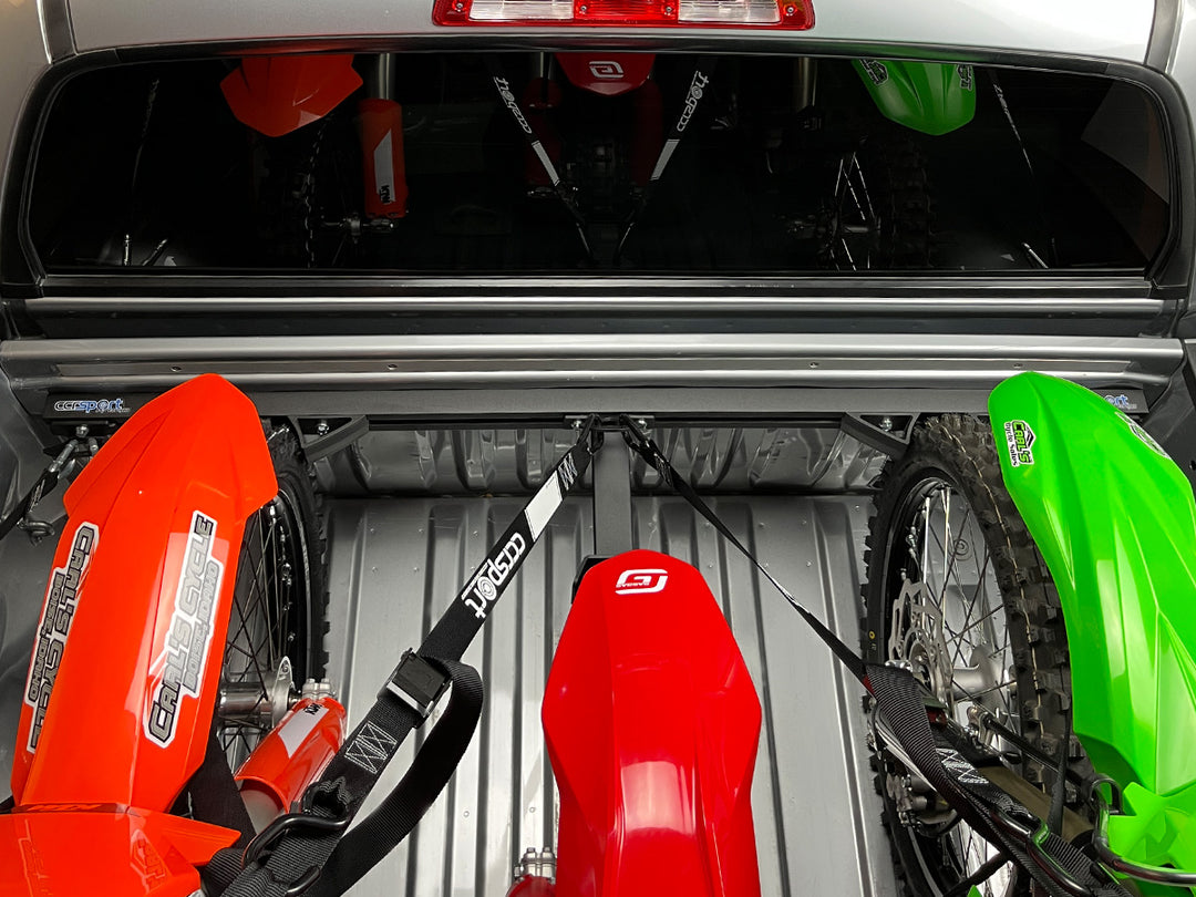 Three full size off road motorcycles tied down to a Hybrid Moto Rack system in the bed of a track.