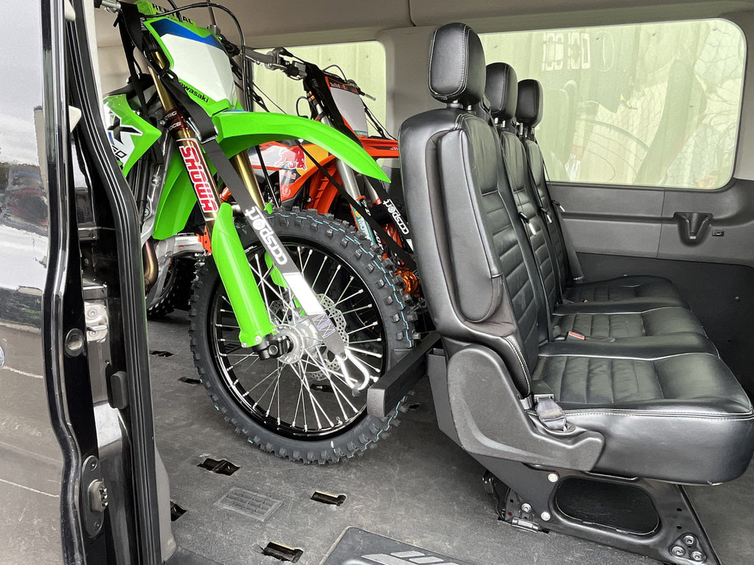 A wide view through the side door of a van showing two motorcycles strapped to the rear passenger seat Hybrid Moto Rack.