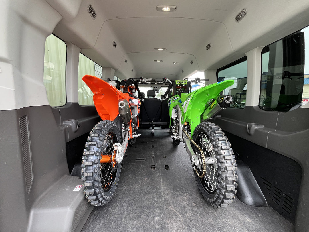 A wide angle rear view of two motocross dirt bikes loaded into the back of a van.