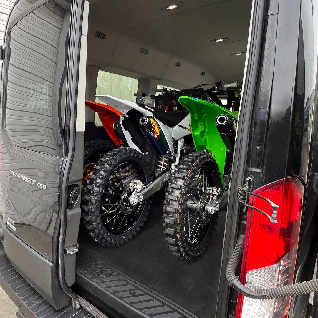 This view shows three full size dirt bikes fitting inside of a Ford Transit van with space to close the rear doors.