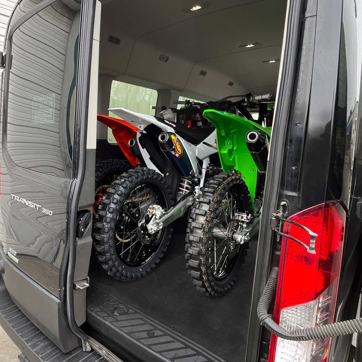 This view shows three full size dirt bikes fitting inside of a Ford Transit van with space to close the rear doors.