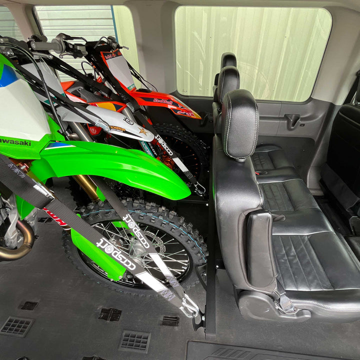 An upper angle side view of three dirt bikes secured to the rear passenger seat of a Ford Transit van using the Hybrid Moto Rack.