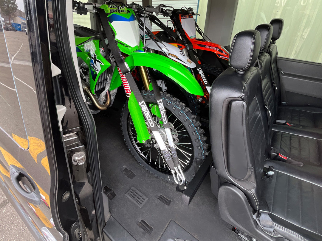 Three motorcycles loaded into a van and secured with tie down straps to the rear passenger seat with a motorcycle carrier rack.