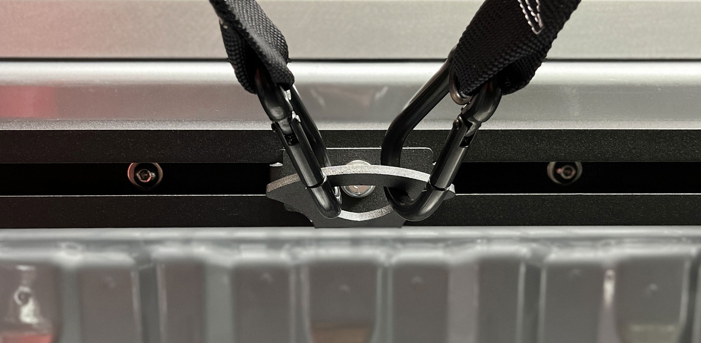 Close-up of a truck bed tie down anchor with two tie down straps attached with carabiner hooks.