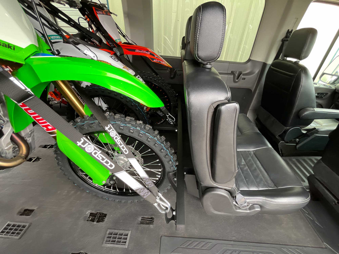 Three motocross dirt bikes tied down to a motorcycle support rack in the back of a van.