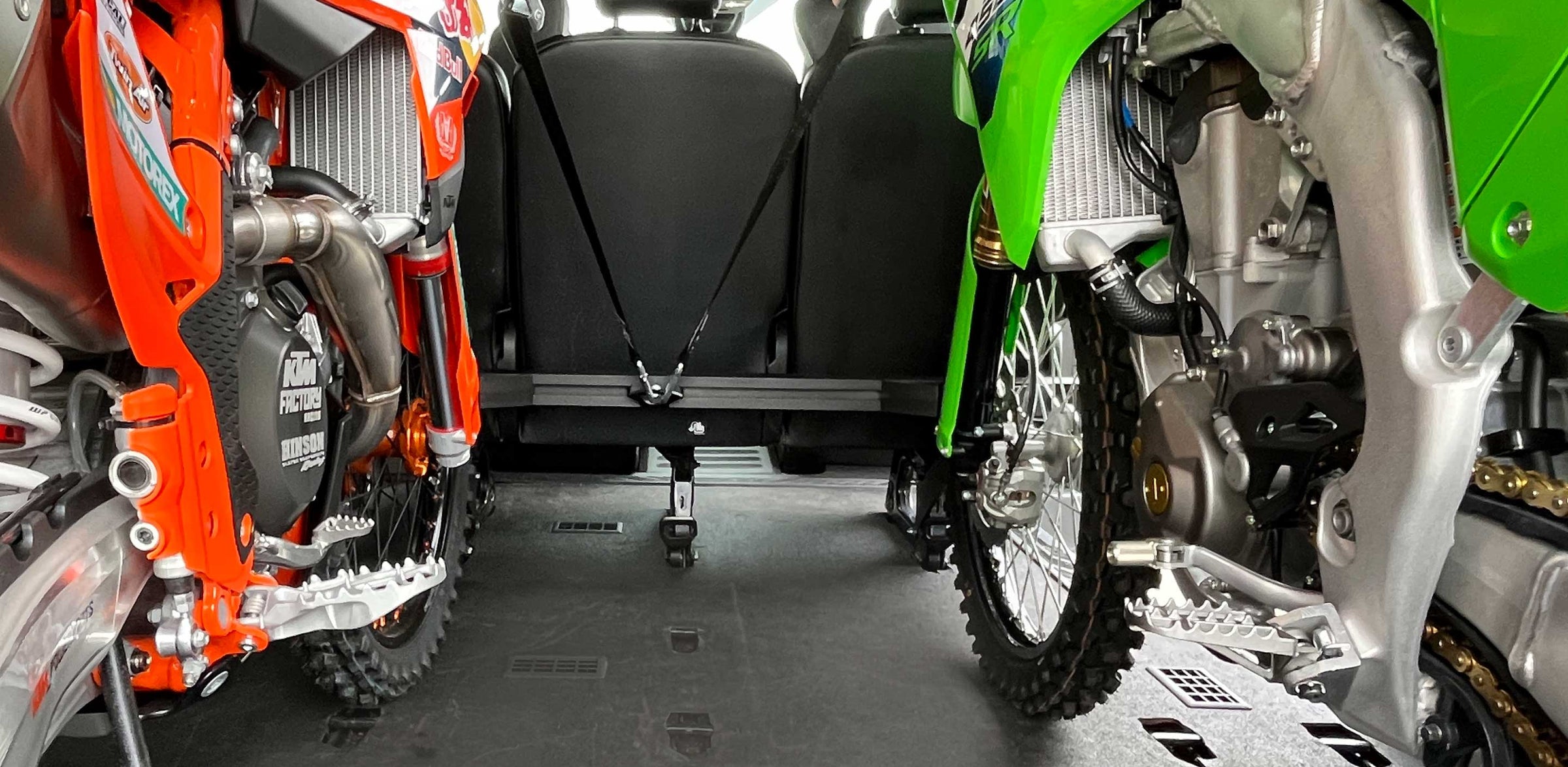 A Kawasaki and KTM motocycle strapped into a van with the Hybrid Moto Rack that mounts to the rear bench passenger seat of the van.