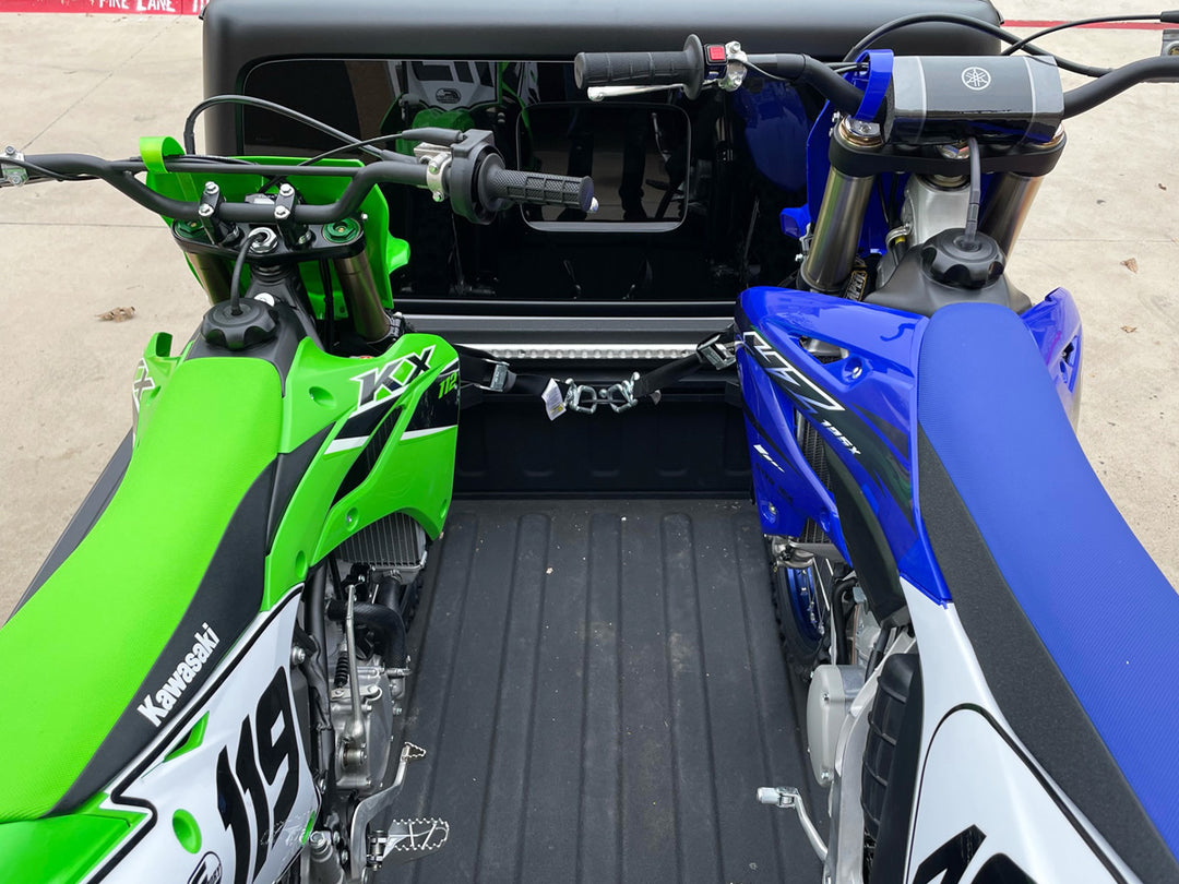 Two off-road motorcycles secured in a Jeep Gladiator truck bed using a CCR Sport motorcycle transport system.