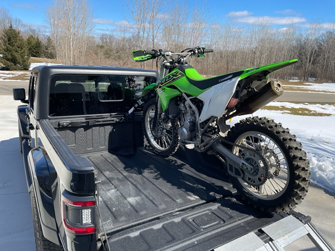 A Jeep Gladiator truck outfitted with a Hybrid Moto Rack and a Kawasaki dirt bike tied down for transport.