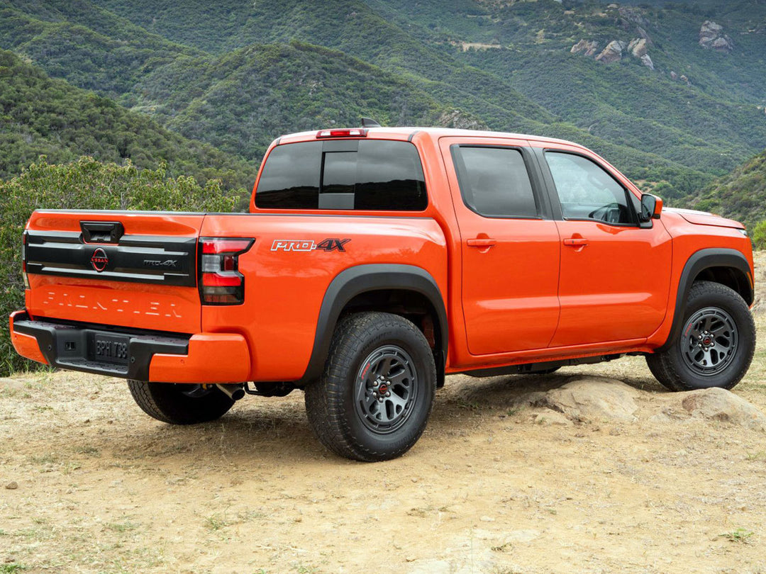 Red Nissan Frontier Pro 4X parked on a hill with green mountains in the background.