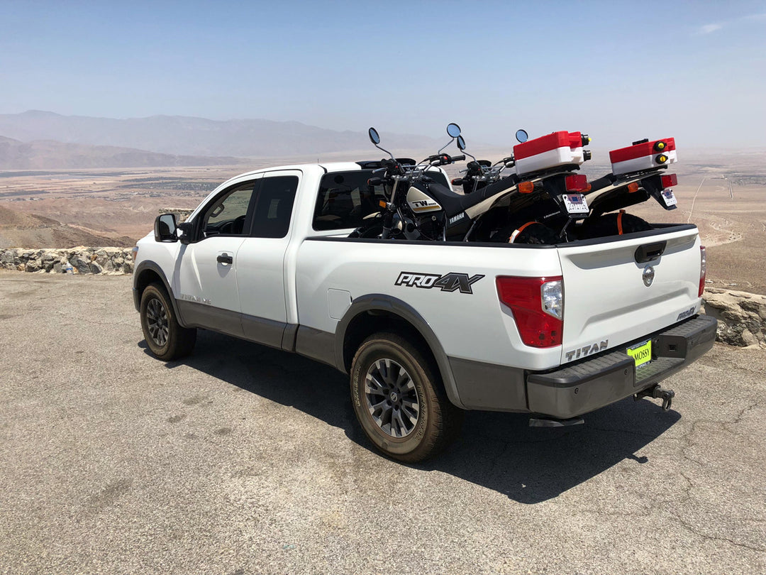 A Nissan Titan Pro 4X truck with two trail motorcycles loaded in the truck bed with scenic view backdrop.