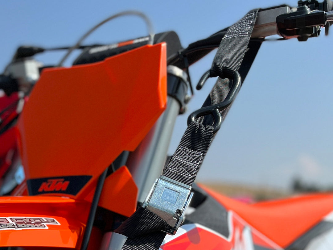 Detailed image showing tie down strap S-hook and soft tye loop holding a motorcycle handlebar.