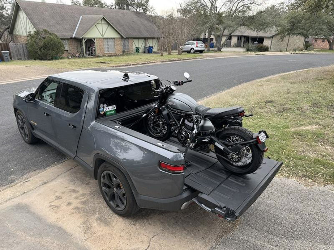 A grey Rivian truck with a grey Ducati street bike loaded in the trucks cargo bed using the CCR Sport Hybrid Moto Rack system.
