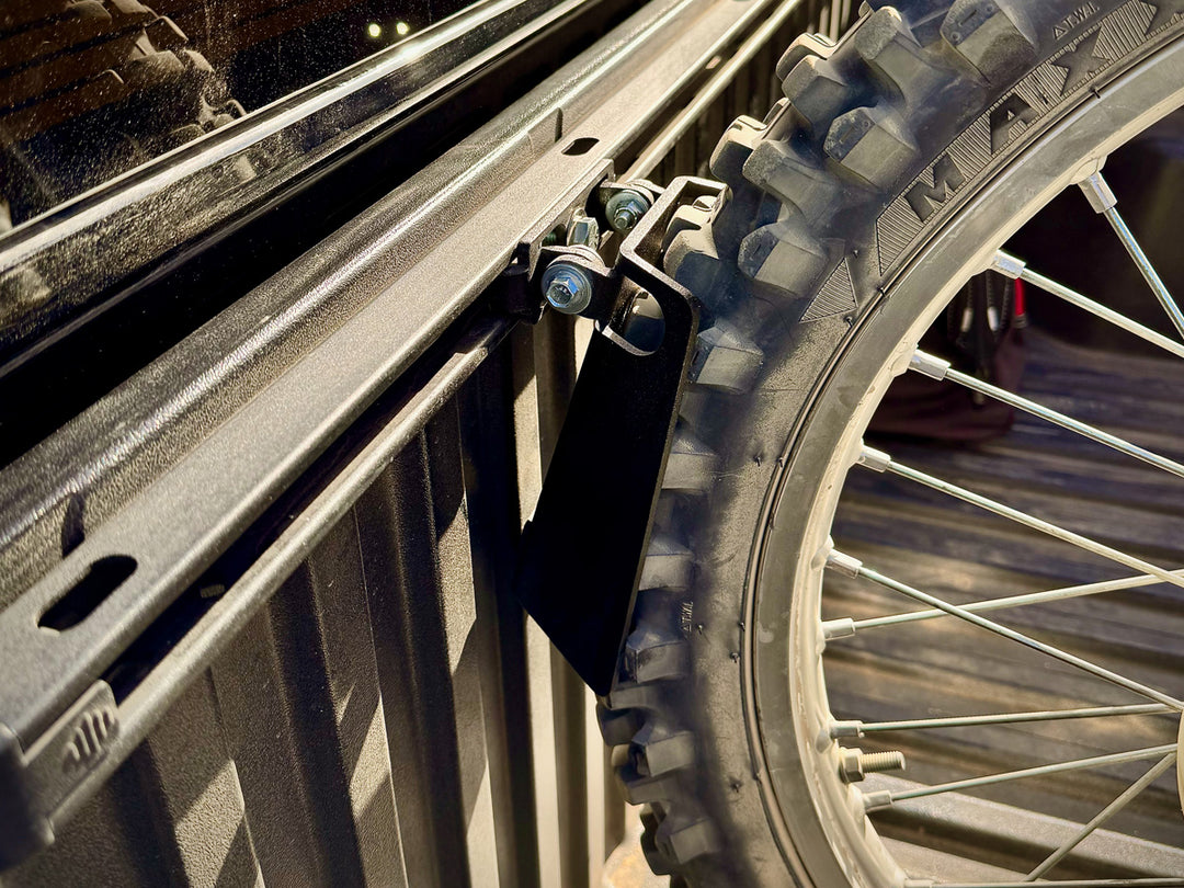 Close-up image of a knobby tire of a dirt bike positioned in a motorcycle wheel chock mounted to a Toyota truck bed Deck Rail.