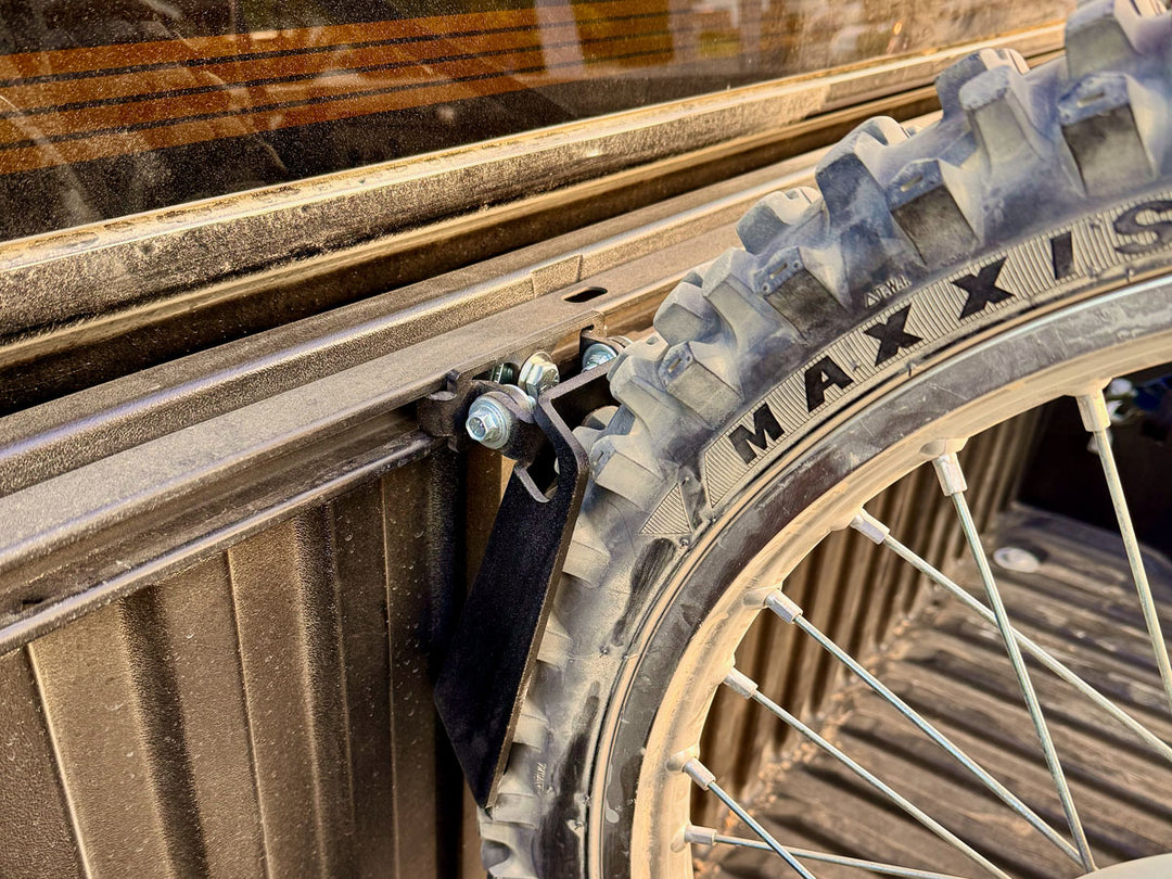 Toyota Deck Rail Pivot Chock mounted in the bed of a Toyota truck with a knobby dirt bike tire in the chock.