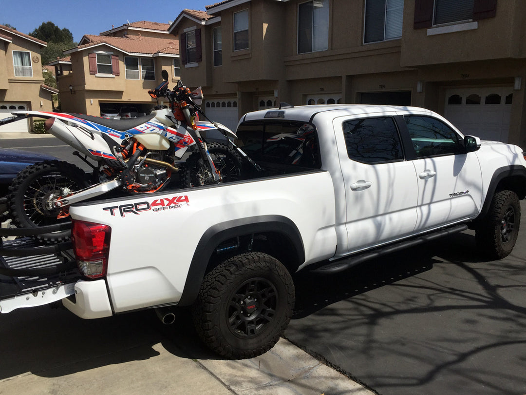 A dual-sport motorcycle loaded into the bed of a white Toyota Tacoma pickup.