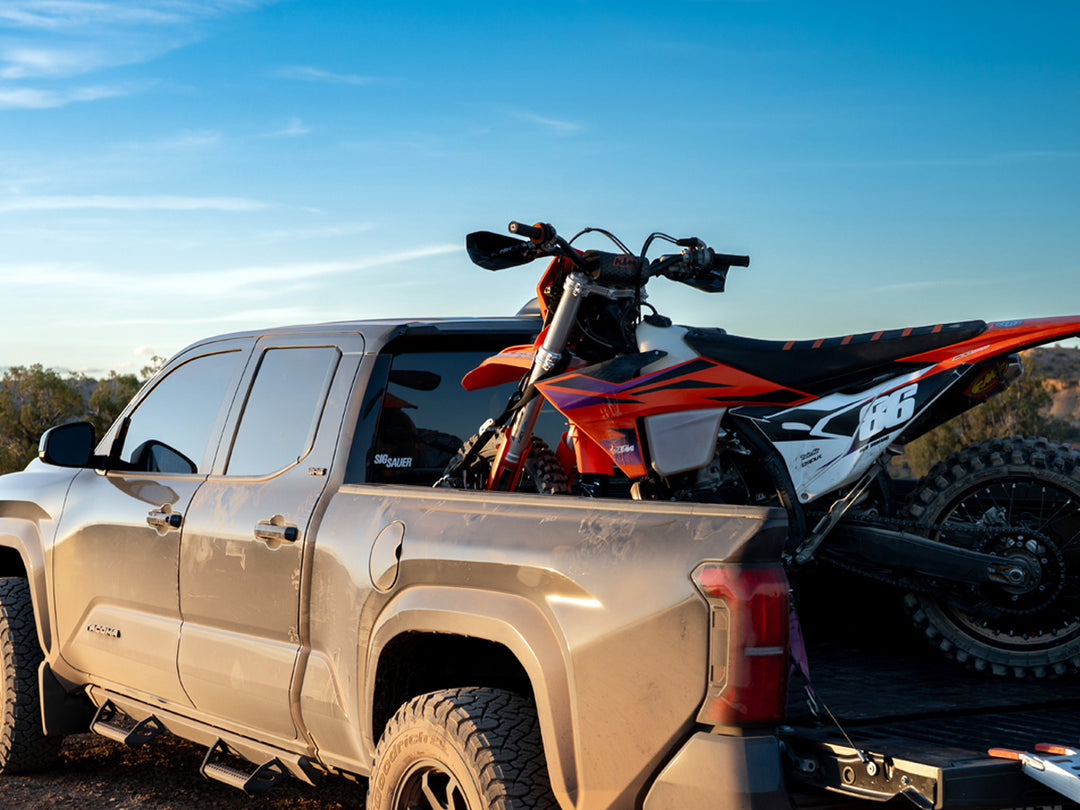 A dirt bike motorcycle in the bed of a Toyota Tacoma with a desert back drop.