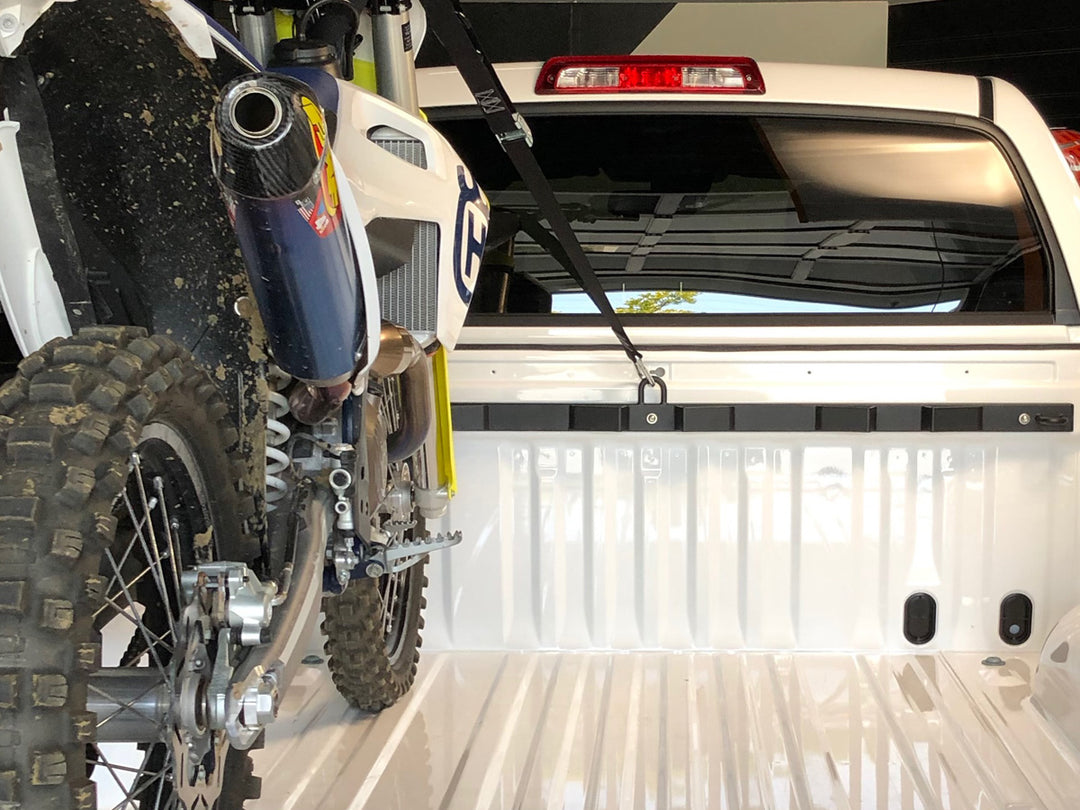 A clean image of a white truck outfitted with the CCR Sport Bed Buddy Moto Rack and a Huqvarna dirt bike strapped in for transport.