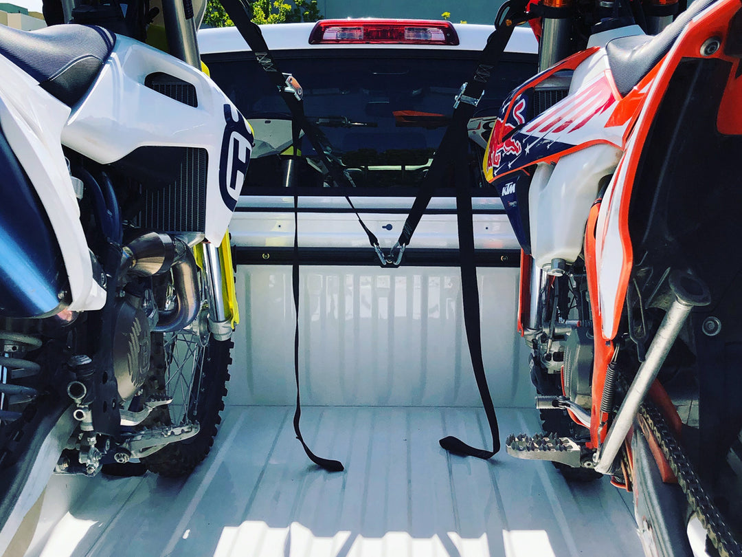 A KTM and Husqvarna loaded in the bed of a truck with tie down rack system by CCR Sport.