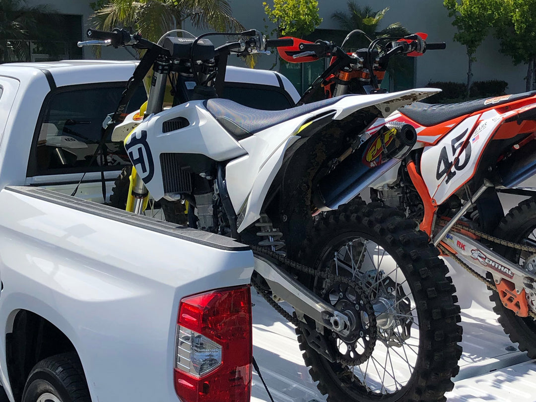 Two dirt bikes loaded in the bed of a truck ready for transport.