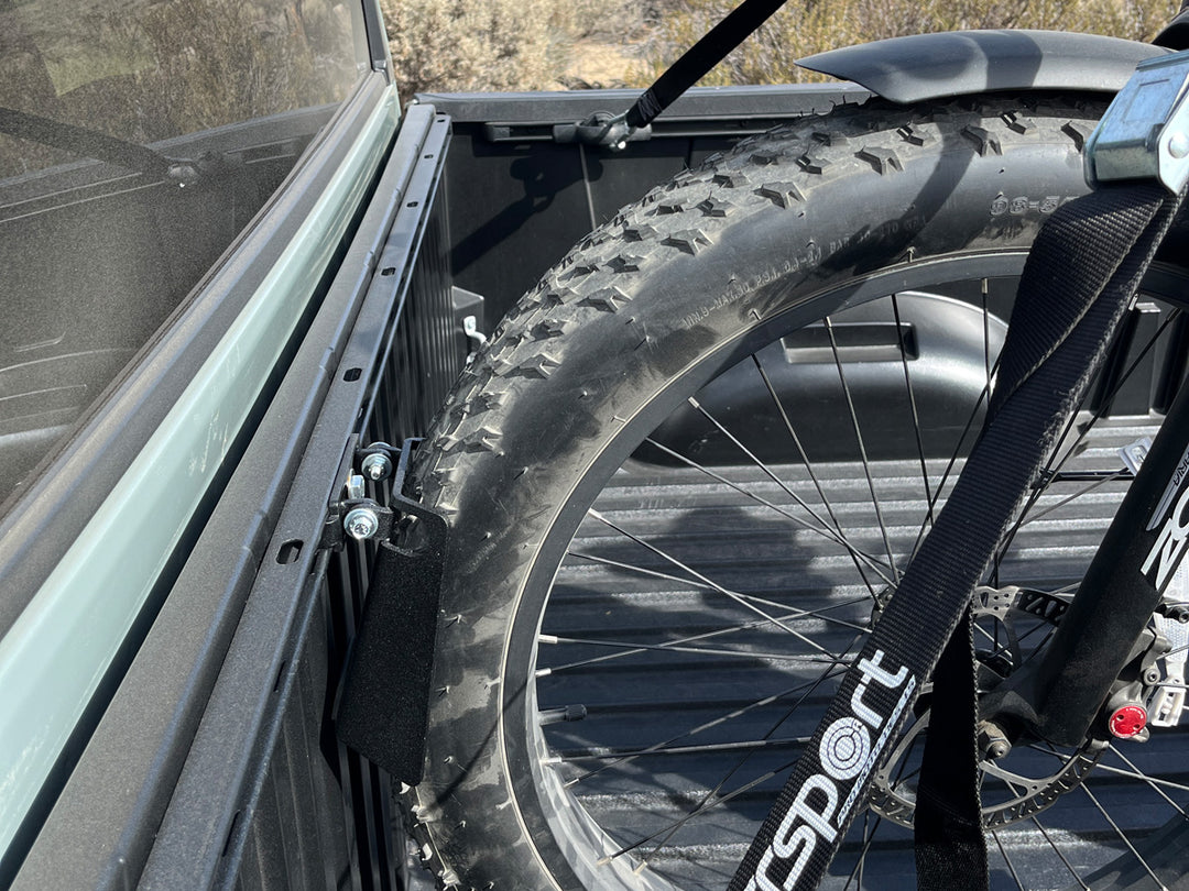 A close-up side angle of the front tire of a fat tire ebike stabilized for truck bed transport using the CCR Sport Toyota Deck Rail Pivot heel Chock.