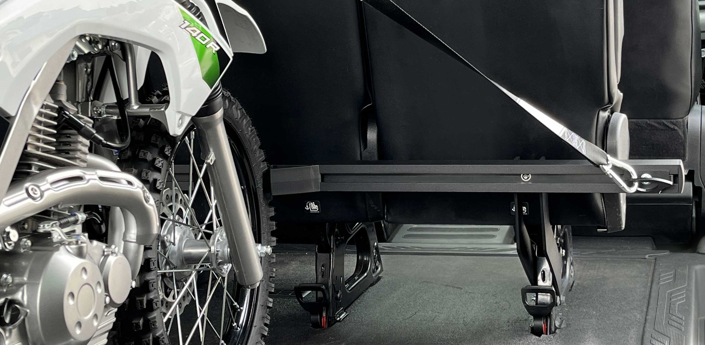 A single dirt bike loaded into the back of a moto van and tied down to a rear bench seat mounted motorcycle tie down rack.