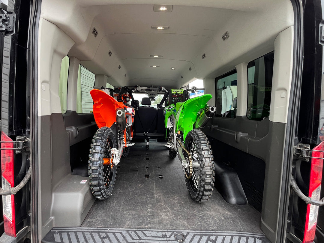 Two off-road motorcycles secured inside a Ford Transit van using the CCR Sport Hybrid Moto Rack System with passenger seating installed.