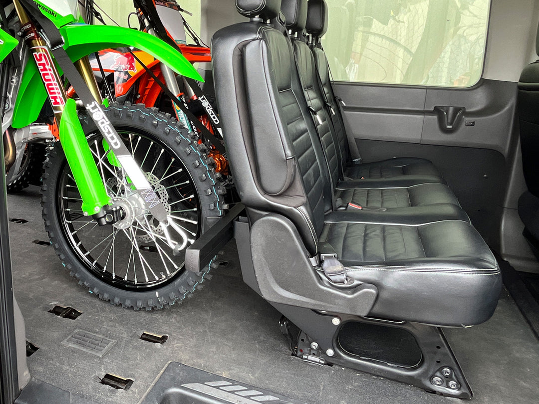 Off-road motorcycles secured behind passenger seating inside a Ford Transit van using the CCR Sport Hybrid Moto Rack System.